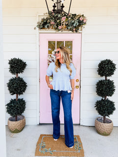 Model wearing dark-wash Risen wide leg jeans with crease-line detail and a light blue knit top.